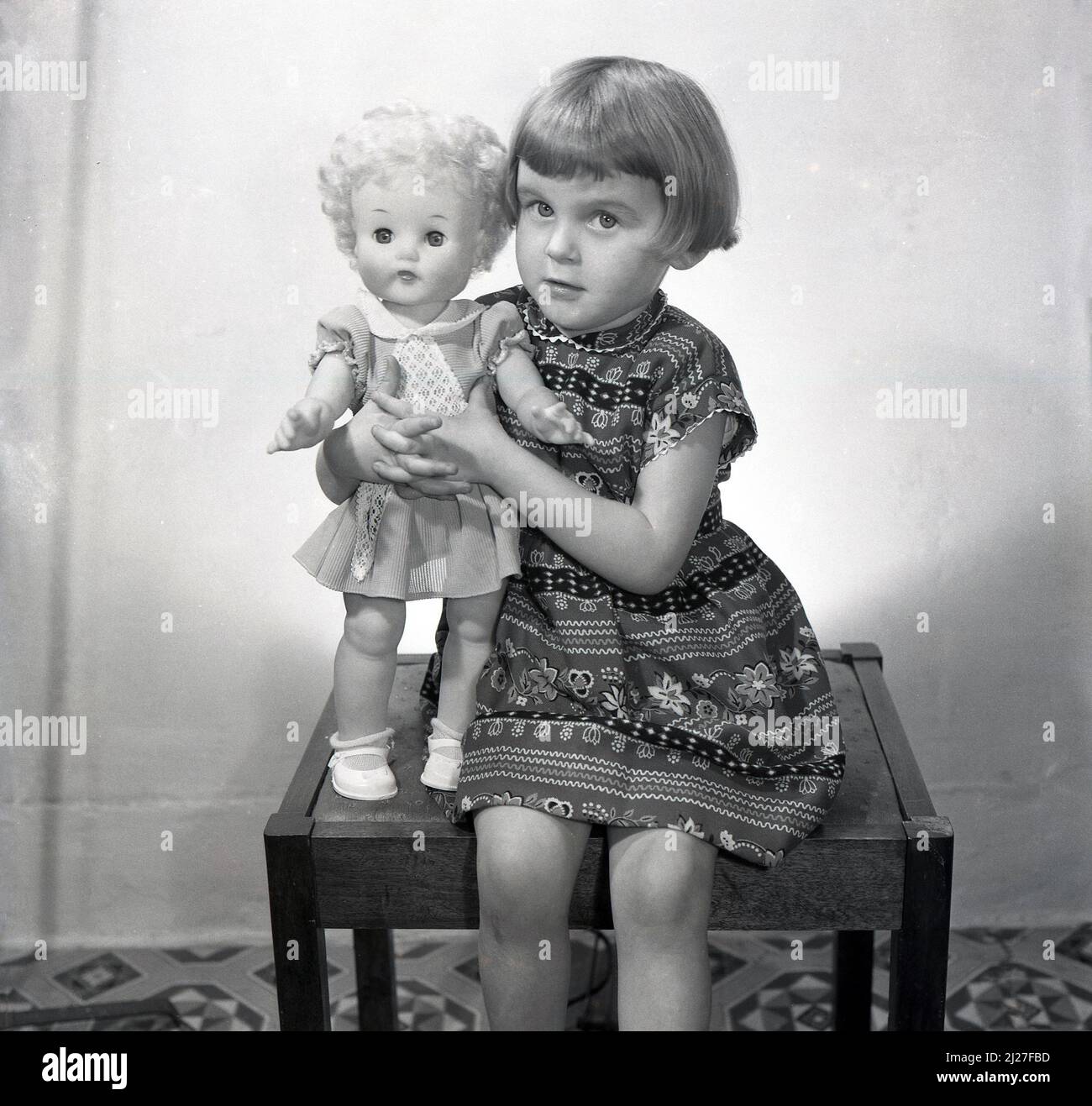 1960, storica, una bambina seduta su uno sgabello per una foto che tiene la sua bambola giocattolo, Inghilterra, Regno Unito. Foto Stock