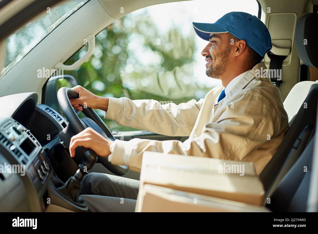 HES un autista scatola di cartone. Colpo di un uomo felice di consegna che guida il suo furgone con le scatole nel sedile anteriore. Foto Stock