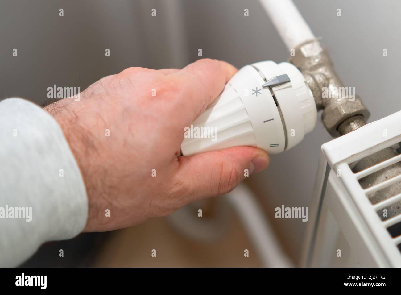 Man Hand regola la manopola di regolazione della temperatura del radiatore di riscaldamento per ridurre i costi di riscaldamento. Foto Stock