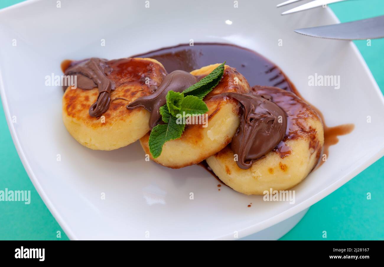 Porzione di cheesecake su un piatto bianco con salsa di cioccolato e condimento. Pancake al curd con menta. Cibo al forno. Vista dall'alto della colazione. Cheesecake. Foto Stock