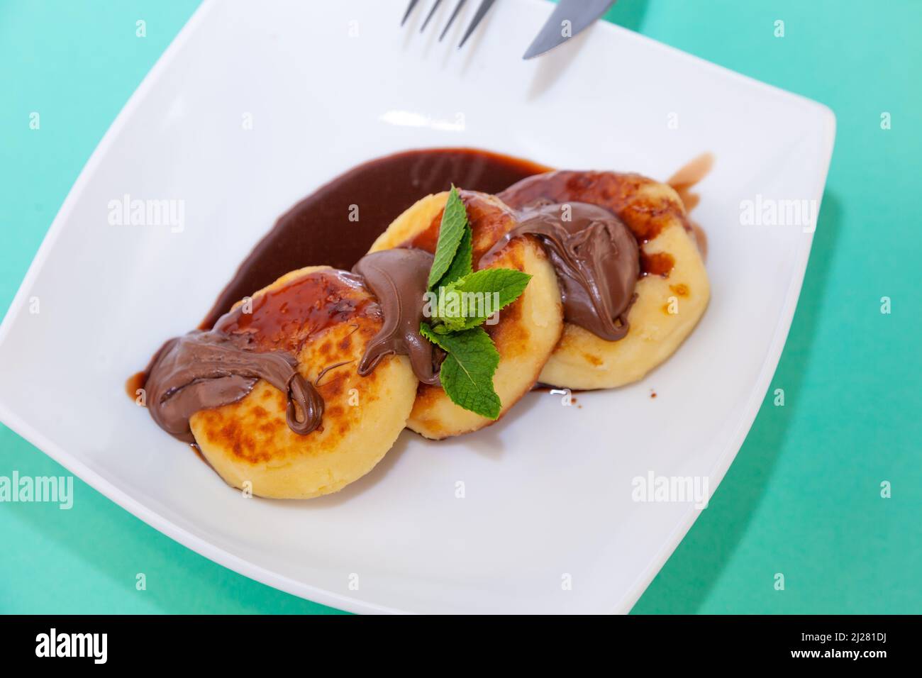 Porzione di cheesecake su un piatto bianco con salsa di cioccolato e condimento. Pancake al curd con menta. Cibo al forno. Vista dall'alto della colazione. Cheesecake. Foto Stock