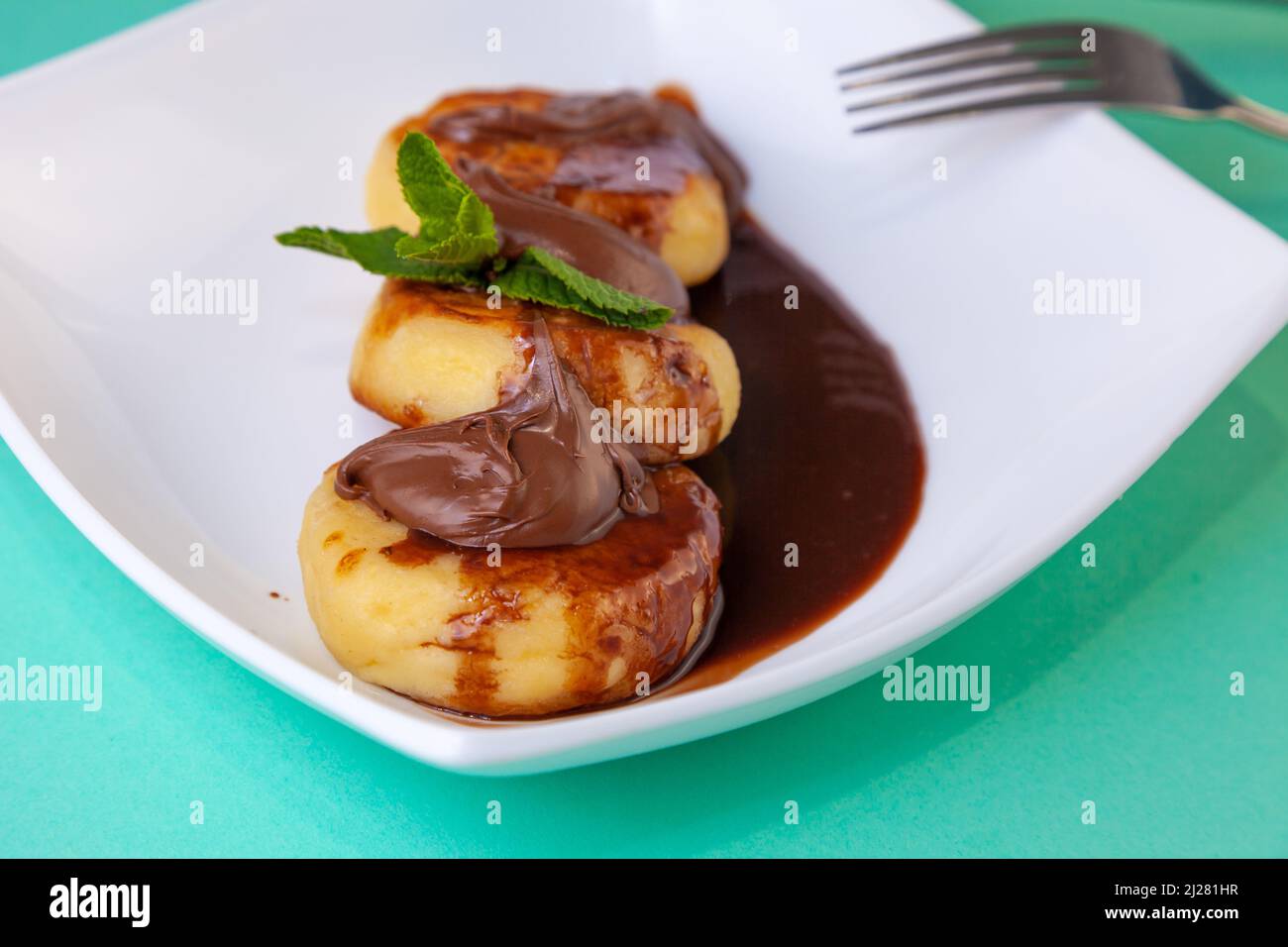 Porzione di cheesecake su un piatto bianco con salsa di cioccolato e condimento. Pancake al curd con menta. Cibo al forno. Vista dall'alto della colazione. Cheesecake. Foto Stock