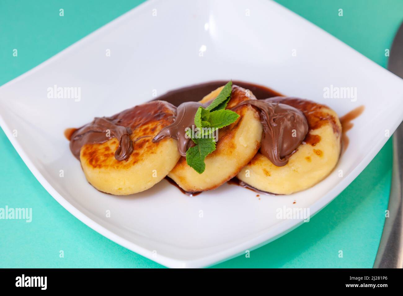 Porzione di cheesecake su un piatto bianco con salsa di cioccolato e condimento. Pancake al curd con menta. Cibo al forno. Vista dall'alto della colazione. Cheesecake. Foto Stock