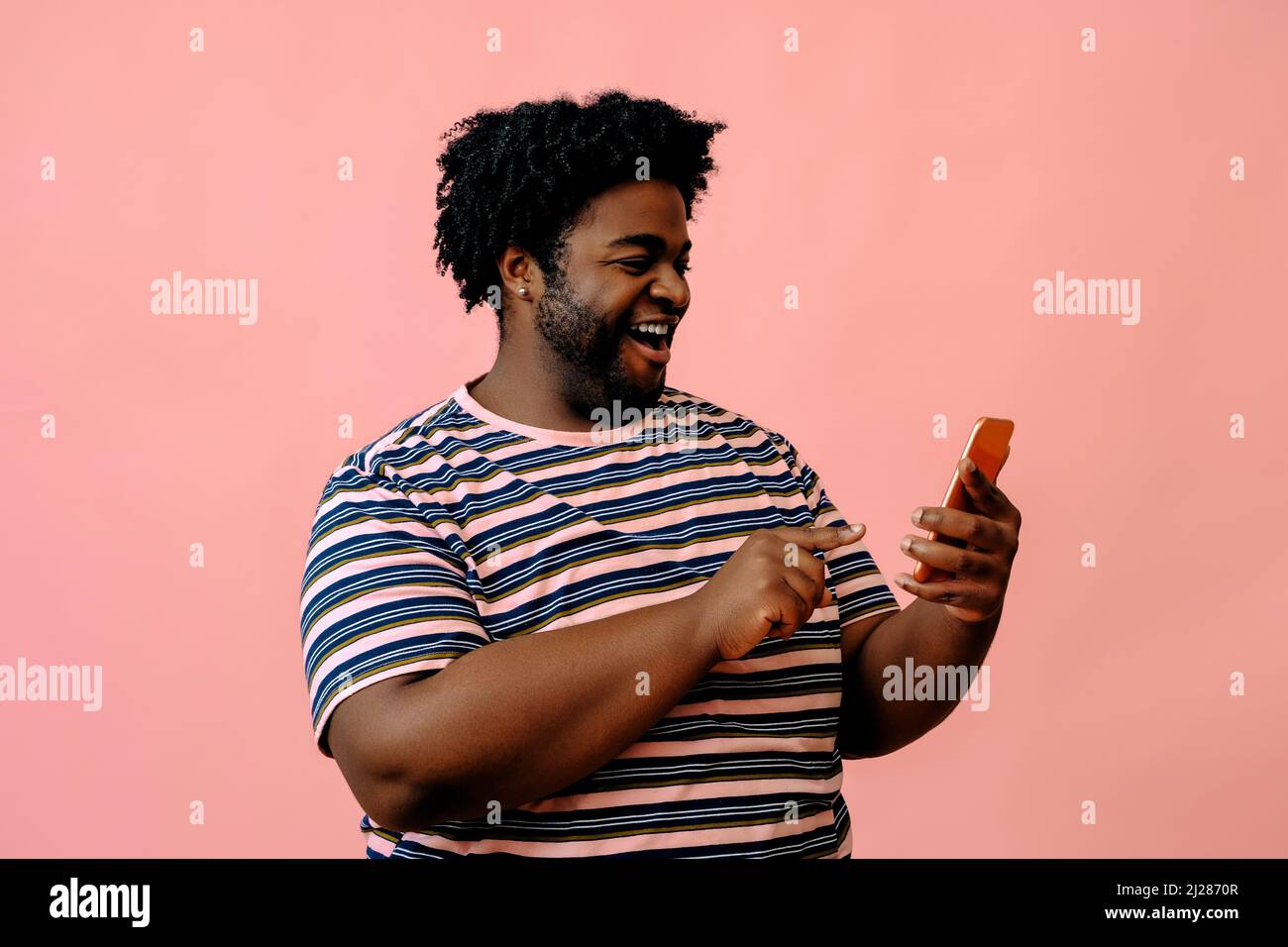 giovane uomo afroamericano con un telefono in posa in studio su sfondo rosa modello maschile in posa Foto Stock