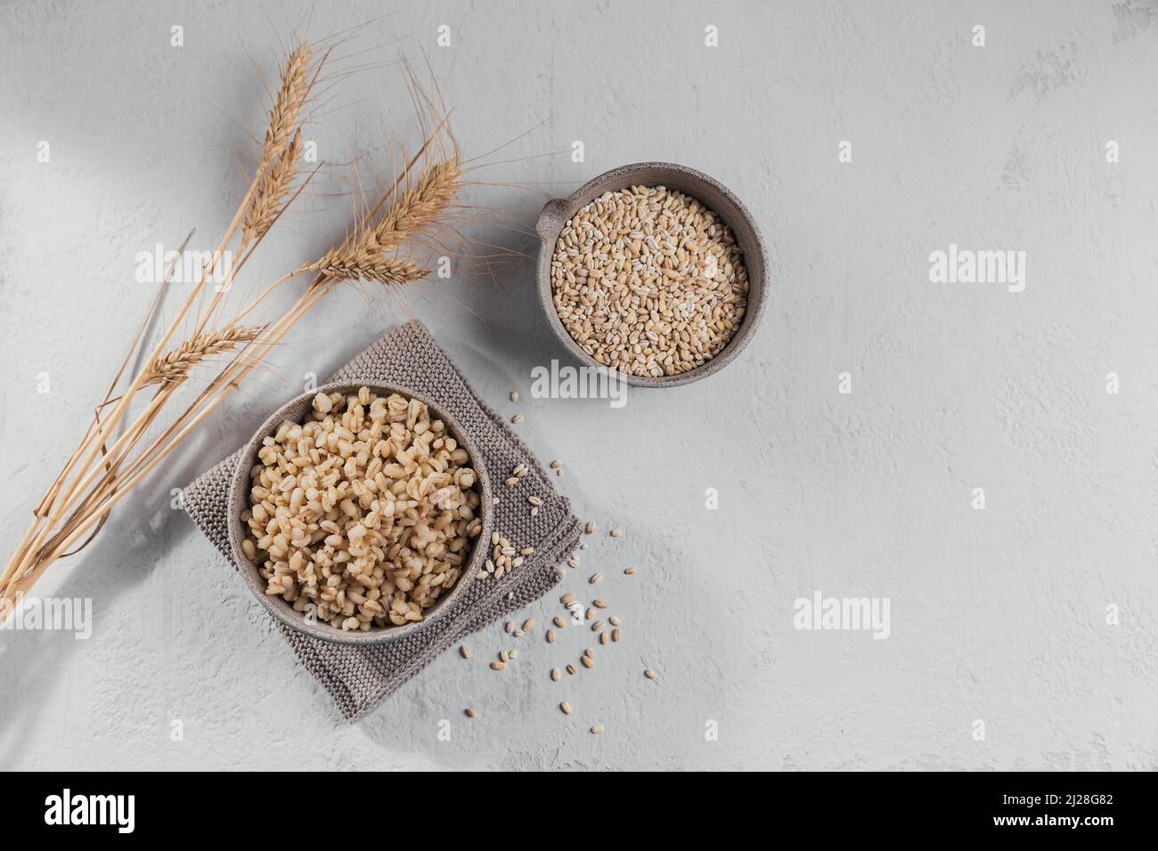 Grano di cereale di orzo essiccato crudo organico in una ciotola e porridge di orzo perlato con le orecchie di frumento su sfondo bianco. Concetto di cibo sano e dietetico. Foto Stock