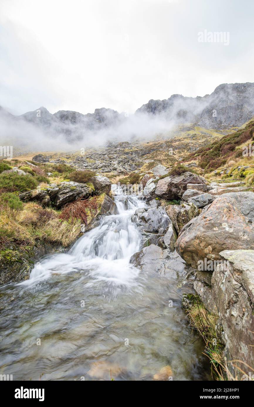 Bassa pov di un ruscello di babbling (che genera una piccola cascata) mentre l'acqua sta scorrendo giù una montagna nebbiosa, Snowdonia National Park, Galles del Nord, Regno Unito. Foto Stock