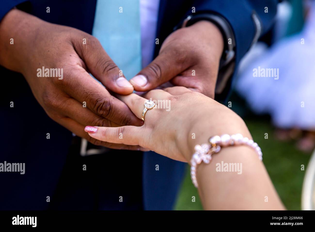 Indossare l'anello di messa sul dito della sposa primo piano di mani e anello Foto Stock
