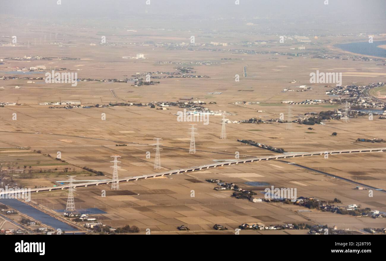 Linea di torri elettriche attraverso terreni agricoli dorati e torbidità Foto Stock