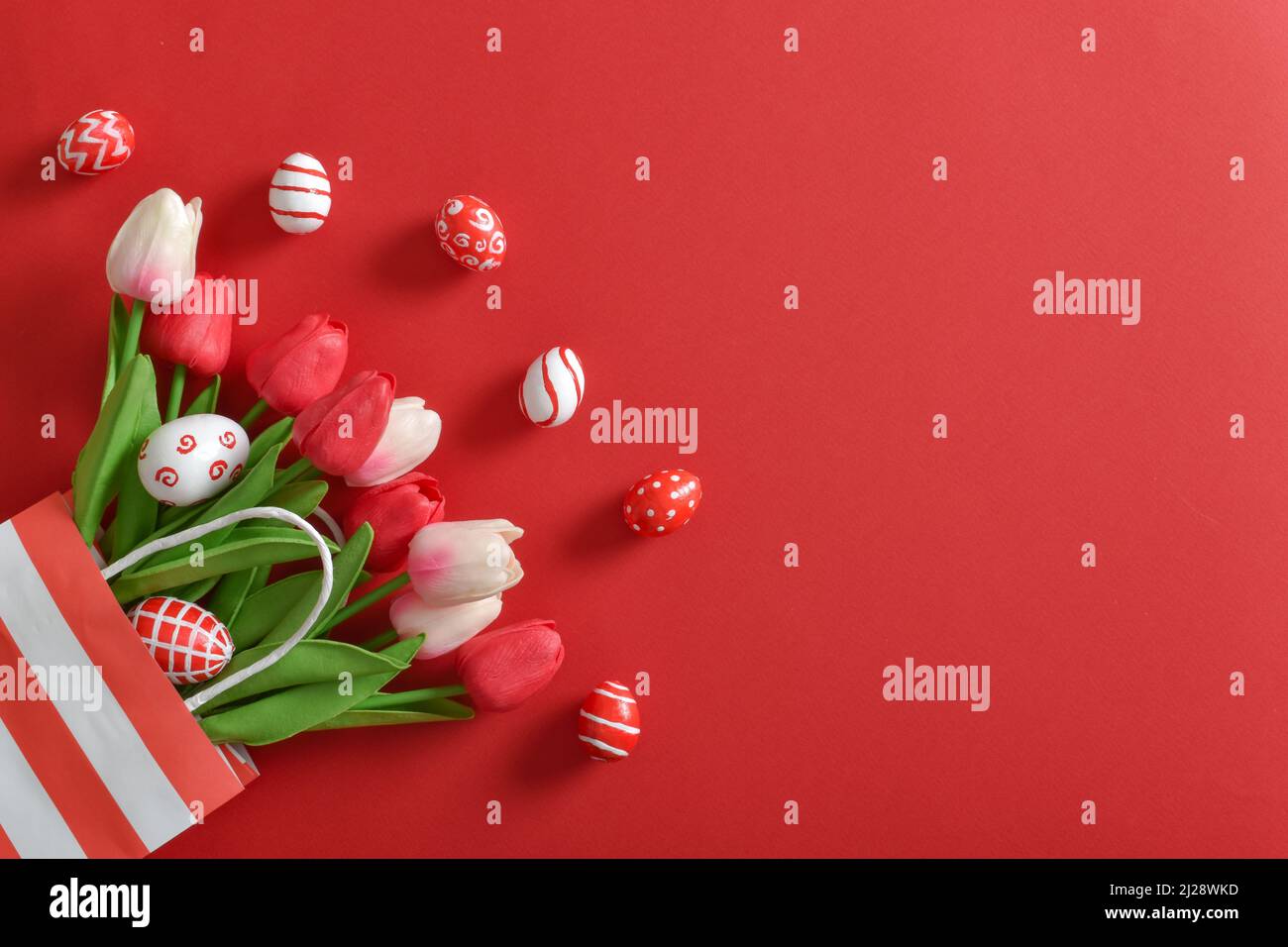 Un bel bouquet di tulipani in un sacchetto di carta ecologica, con uova di Pasqua dipinte su sfondo rosso. Foto Stock