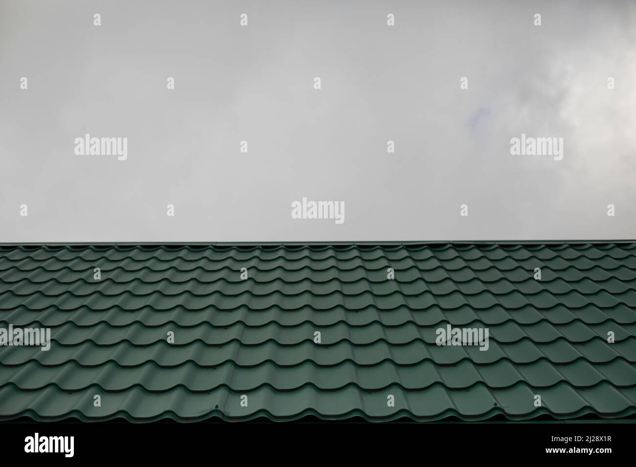 Tetto di casa sullo sfondo del cielo grigio. Tegole verdi. Dettagli dell'architettura. Foto Stock
