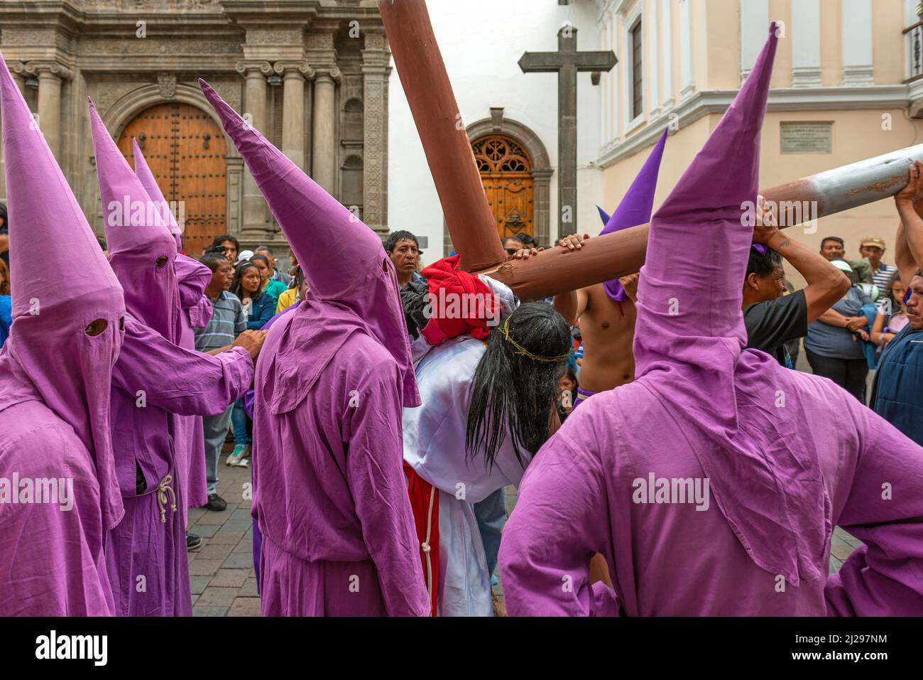 Gruppo di penitenti Cucuruchos in costume viola e Gesù Cristo che porta croce durante la Processione di Pasqua del Venerdì Santo per le strade di Quito, Ecuador Foto Stock