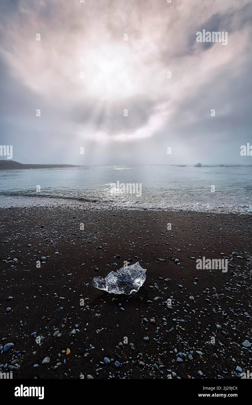 Cristallo di ghiaccio e ciottoli sulla spiaggia di lava nera, illuminata dal sole del mattino, retroilluminazione, raggi di sole attraverso la foschia, Diamond Beach in estate Foto Stock