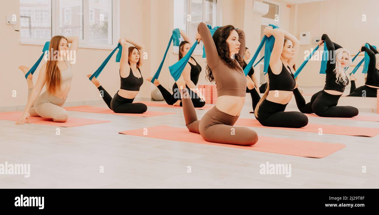 Gruppo di donne di mezza età con istruttore di fitness in leggings sportivi e top, facendo Pilates con il nastro di gomma sul tappeto yoga vicino al Foto Stock