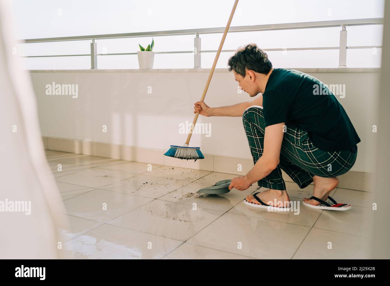 Uomo che pule il pavimento con il mop. Janitor lavare i pavimenti sporchi.  Guy mopping il balcone in una giornata di sole. Persona che fa i chores  domestici. Giovane collega che usa