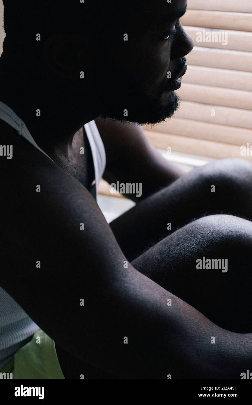 L'uomo che abbraccia le ginocchia e soffre di disturbi mentali a casa Foto Stock