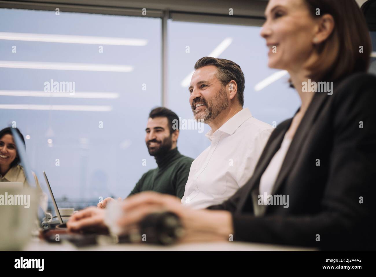 Donna d'affari sorridente con colleghi maschi e femmine che discutono mentre lavorano in ufficio Foto Stock