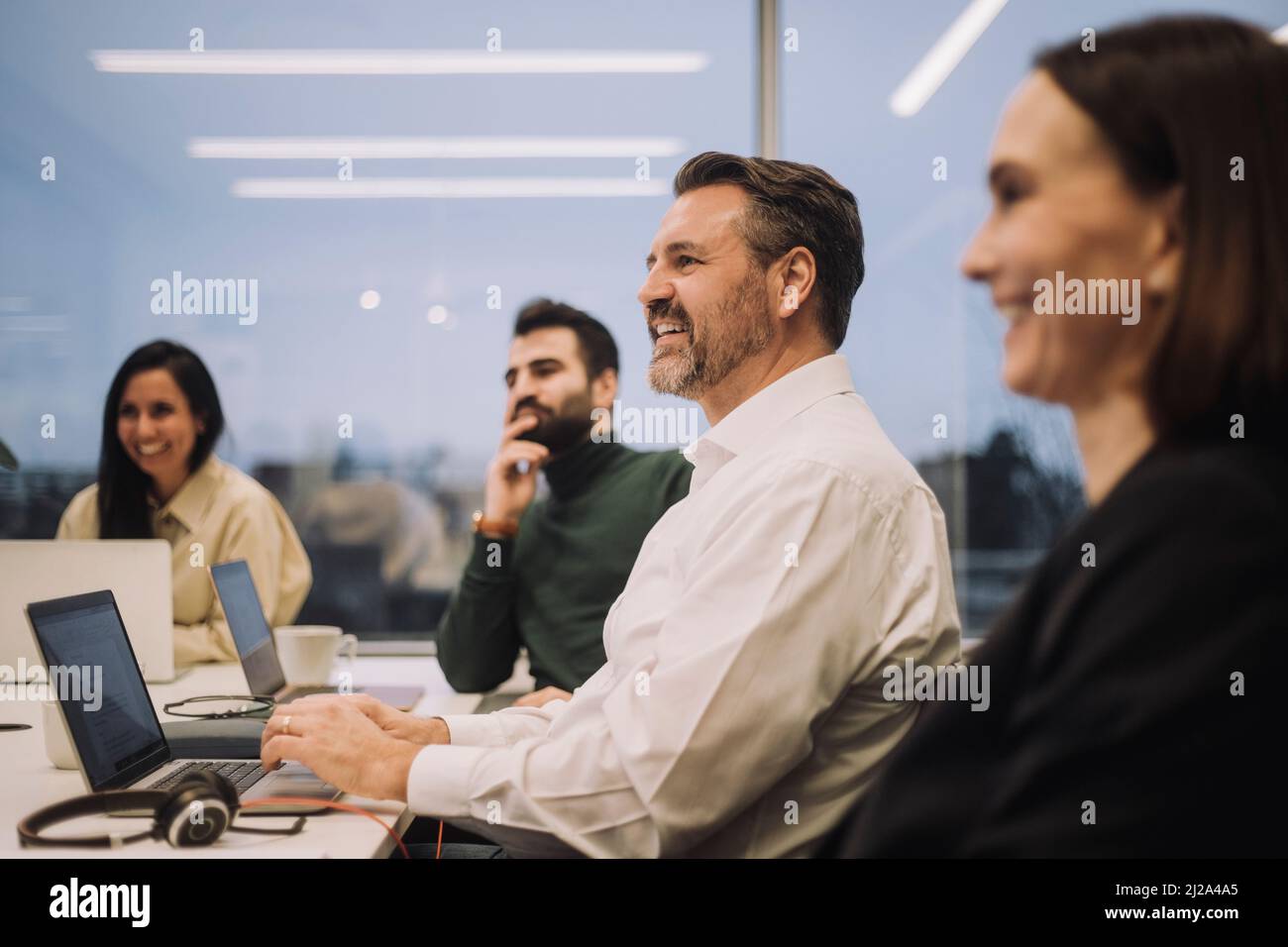 Uomo d'affari sorridente che parla con colleghi maschi e femmine durante l'incontro in ufficio Foto Stock