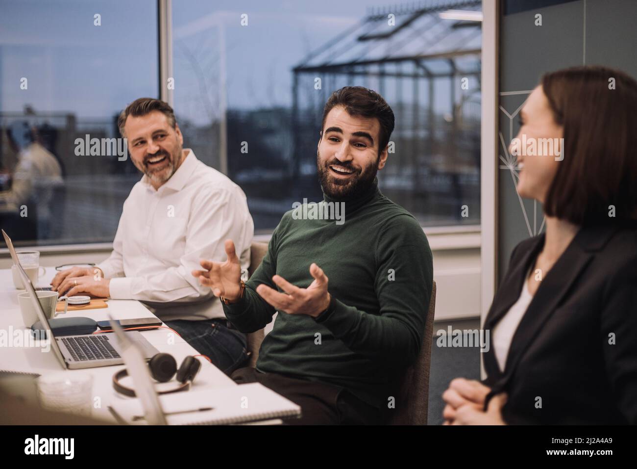 Un uomo d'affari felice che discute con colleghi maschi e femmine in riunione sul posto di lavoro Foto Stock