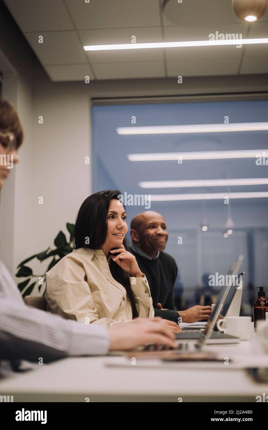 Donna d'affari sorridente con colleghi maschi e femmine che discutono mentre lavorano tardi in ufficio Foto Stock