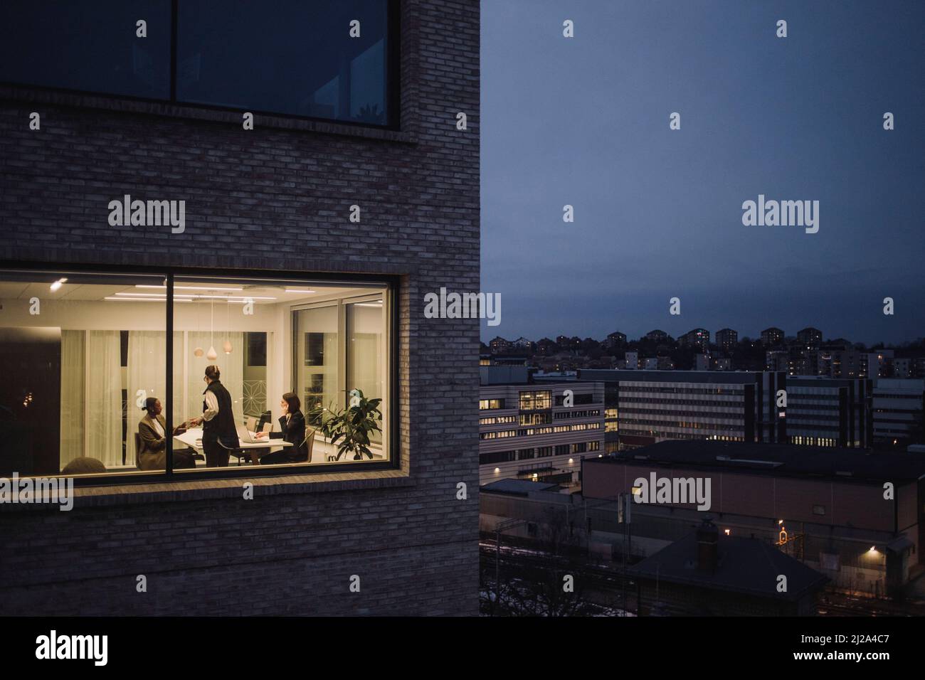 Le colleghe multirazziali femminili che lavorano in ritardo visto attraverso la finestra del posto di lavoro Foto Stock