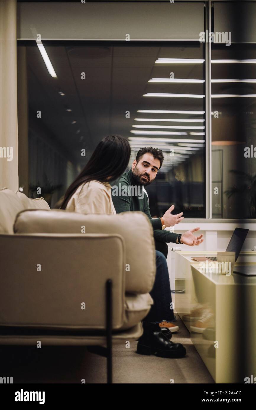 Uomo d'affari che discute di strategia con una collega mentre lavora tardi sul posto di lavoro Foto Stock