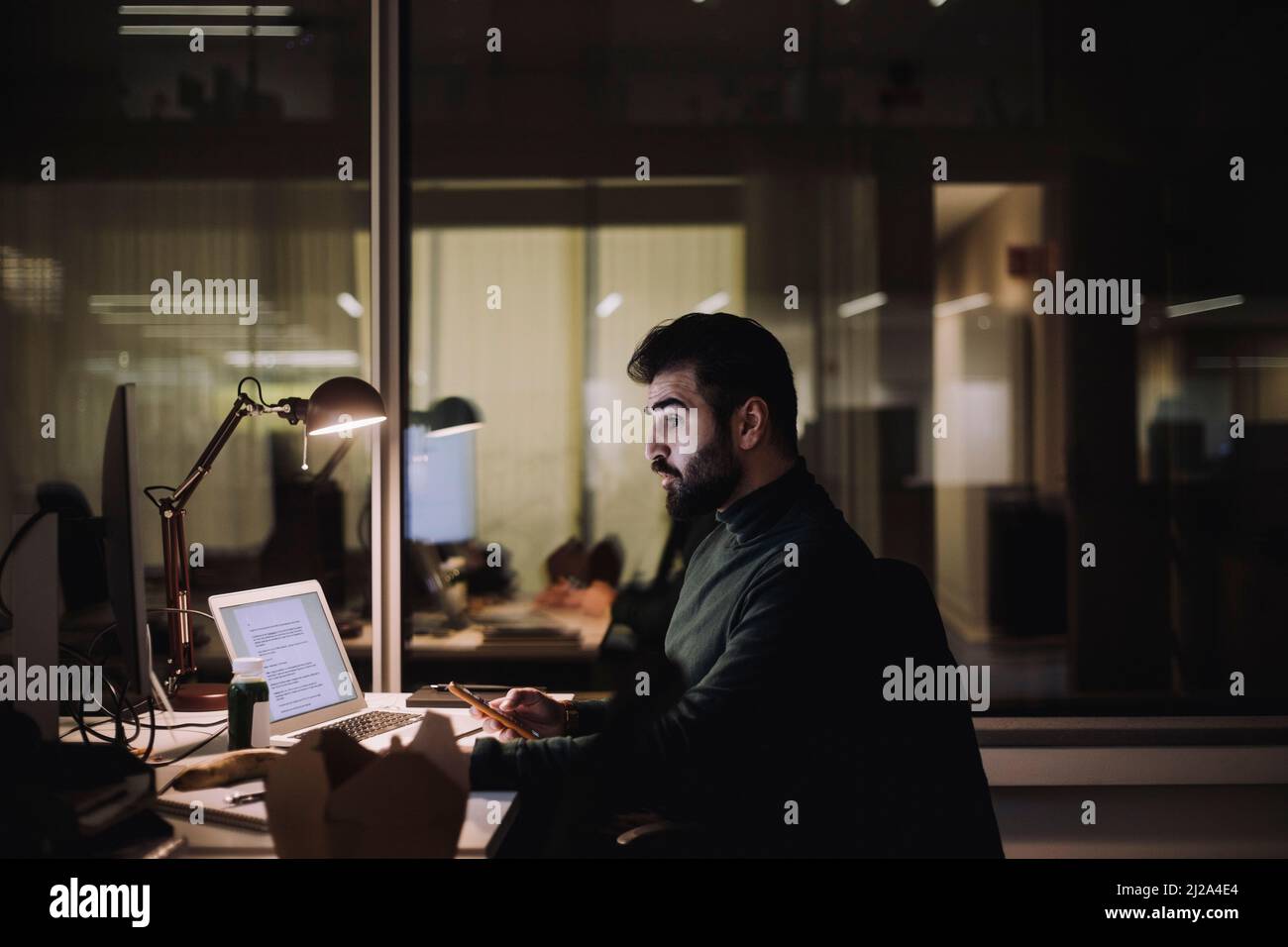 Uomo d'affari con smartphone che lavora sul computer sul posto di lavoro Foto Stock