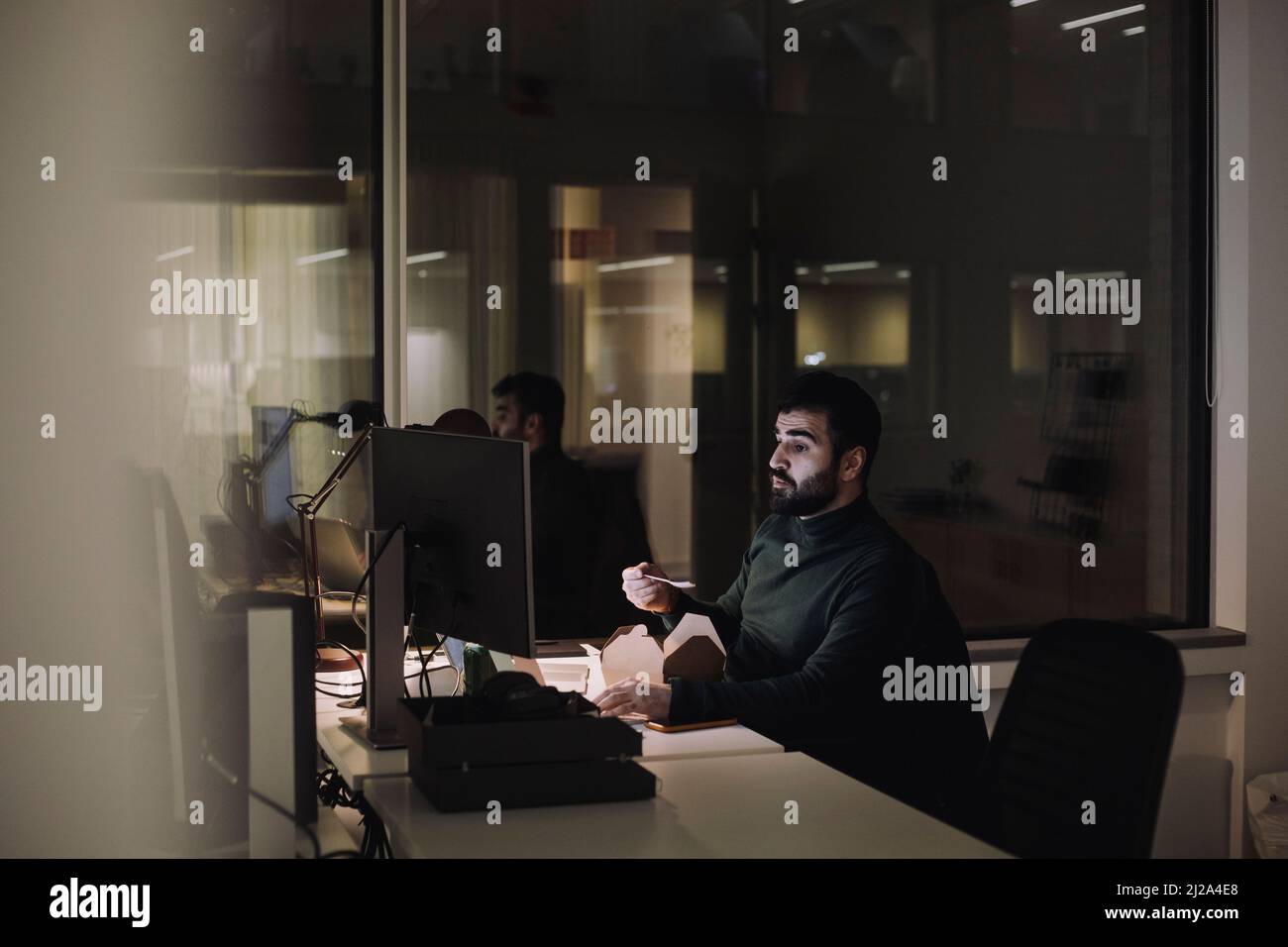 Uomo d'affari adulto medio che mangia mentre lavora tardi in ufficio di notte Foto Stock