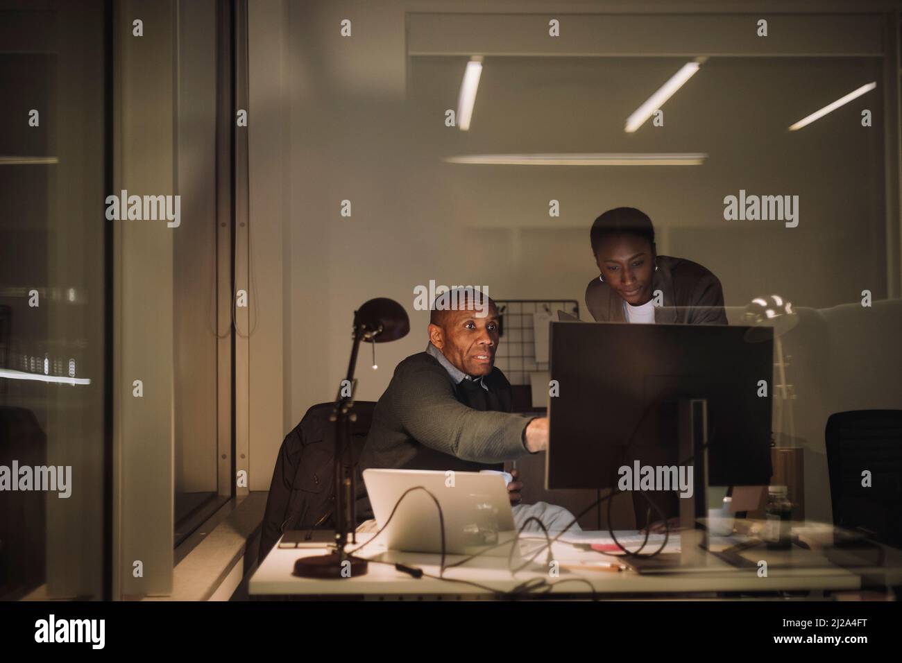 Uomo d'affari maturo che discute con collega femmina sopra il calcolatore in ufficio alla notte Foto Stock