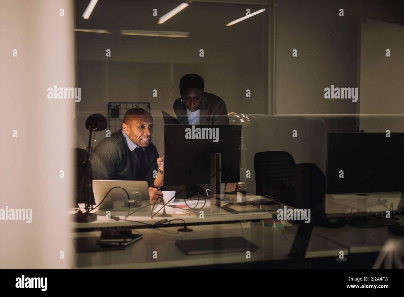 Uomo d'affari che discute con una collega femmina sul computer visto attraverso il vetro sul posto di lavoro Foto Stock