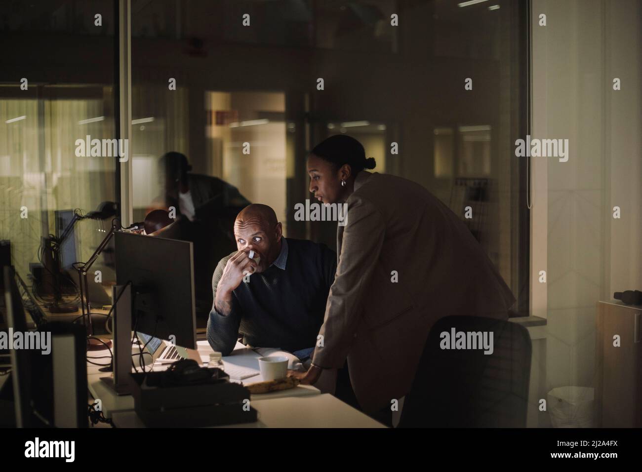Uomo d'affari maturo bere caffè mentre si discute con una collega femmina sul computer in ufficio Foto Stock