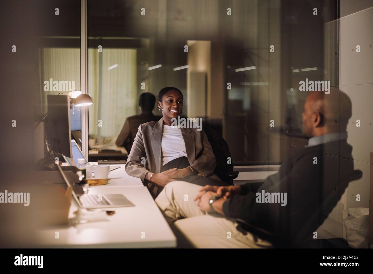 Strategia di pianificazione di una donna d'affari sorridente con un collega di sesso maschile visto attraverso un bicchiere di posto di lavoro Foto Stock