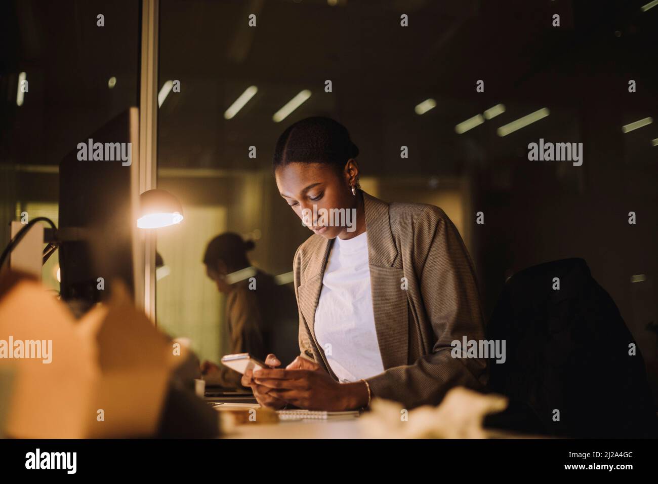 Messaggistica di testo per donna d'affari sullo smartphone mentre si lavora in ufficio di notte Foto Stock