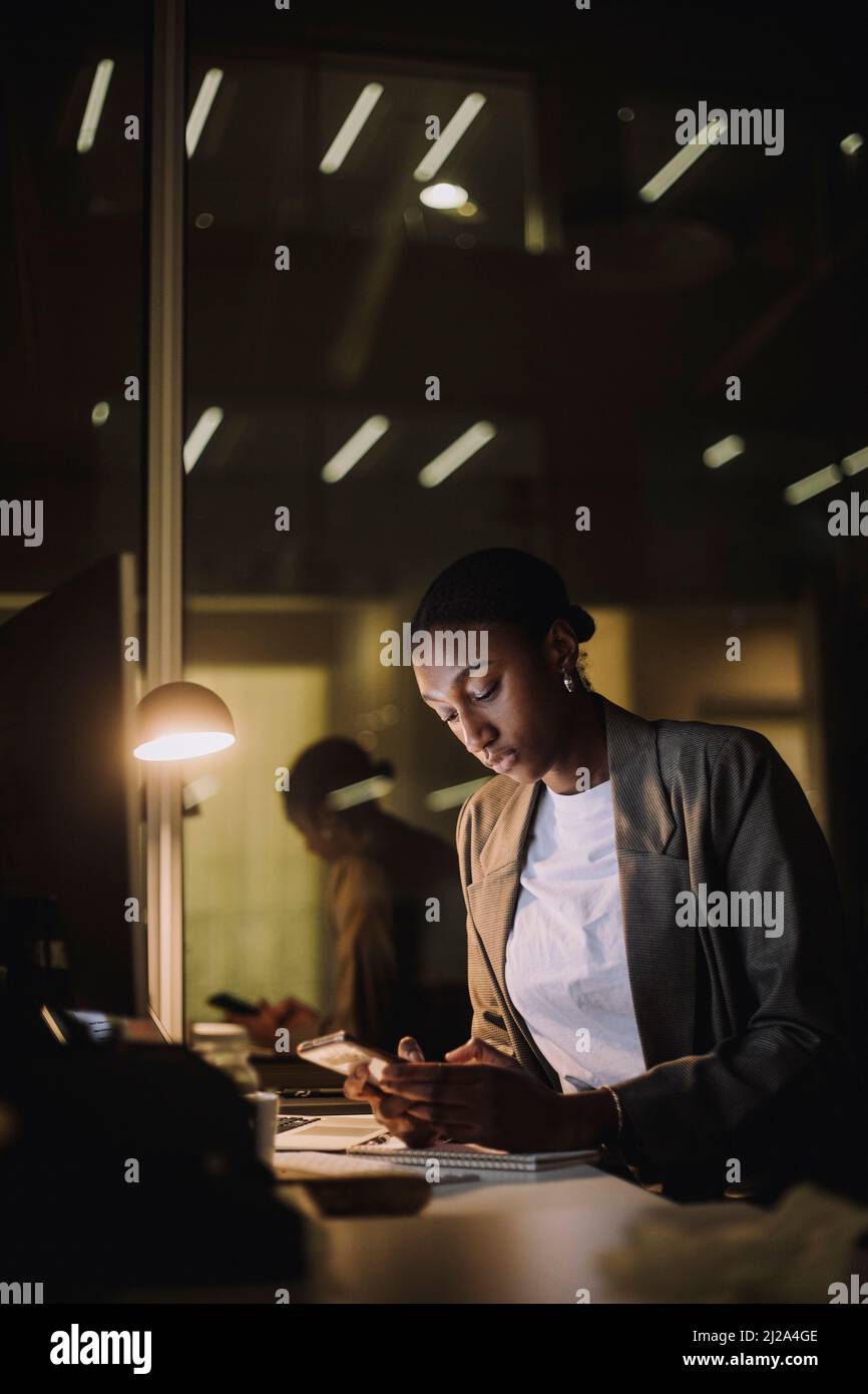 Messaggistica di testo per donna d'affari sul telefono cellulare mentre si lavora tardi sul posto di lavoro Foto Stock