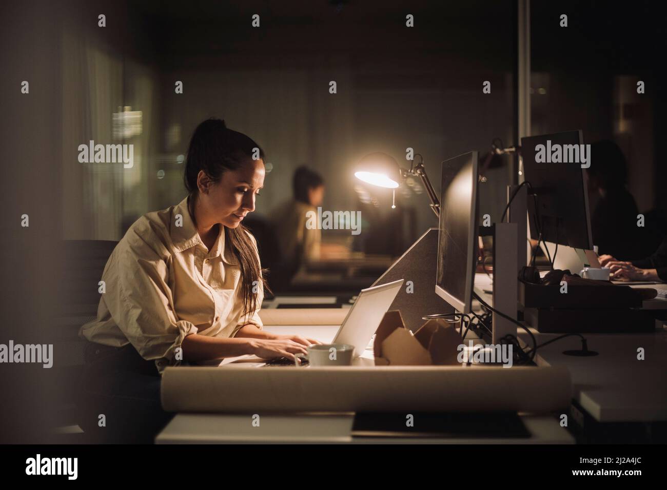 Donna d'affari che si concentra mentre lavora tardi sul laptop in ufficio Foto Stock