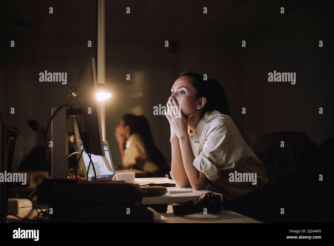 Donna d'affari con le mani che coprono la bocca di lavoro sul computer in ufficio Foto Stock