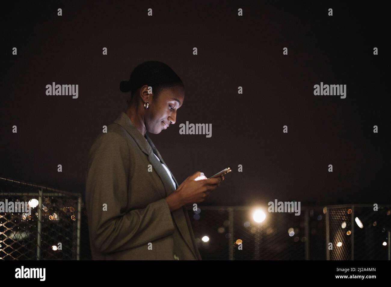 Vista laterale della messaggistica di testo di una donna d'affari sul telefono cellulare di notte Foto Stock