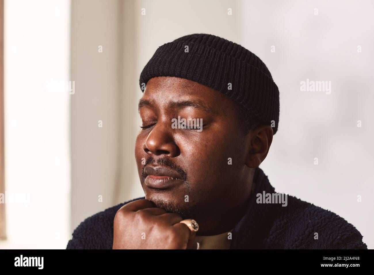 Uomo adulto medio con occhi chiusi e mano sul mento contro la parete Foto Stock