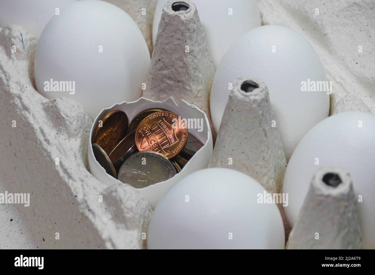 Le uova bianche di pollo sono in una scatola di cartone. Uno di loro è rotto ed è riempito di centesimi americani Foto Stock