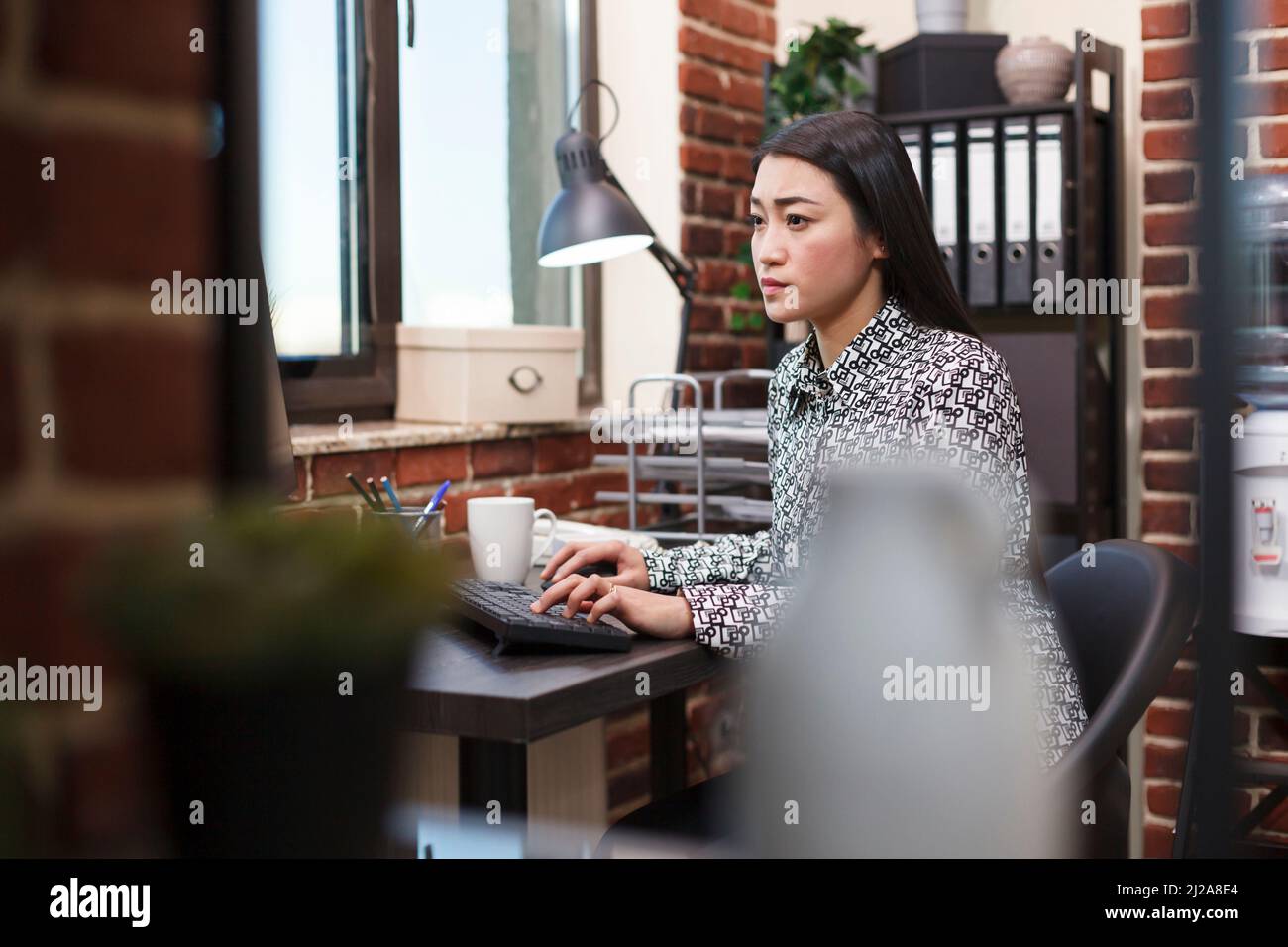 Una donna in ufficio sicura che riassegna idee di marketing di progetto utilizzando il computer di lavoro e seduto alla scrivania. Business woman agenzia finanziaria revisione della strategia di business mentre in ambiente di lavoro. Foto Stock