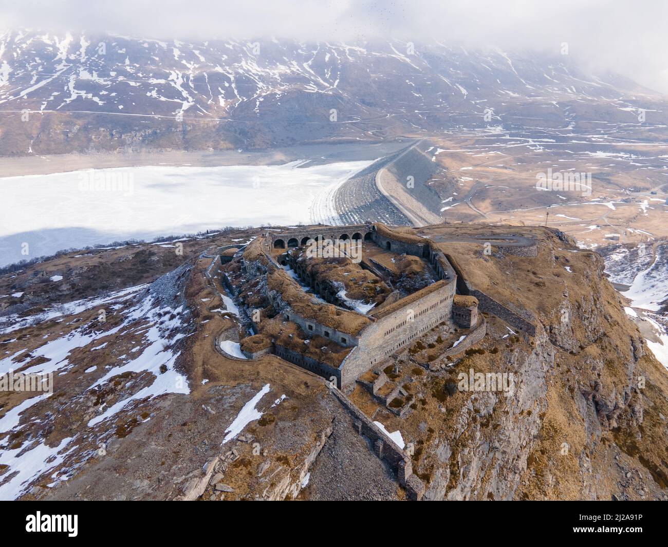 Vista aerea di antiche rovine fortilizio in montagna vicino al lago ghiacciato e diga Foto Stock