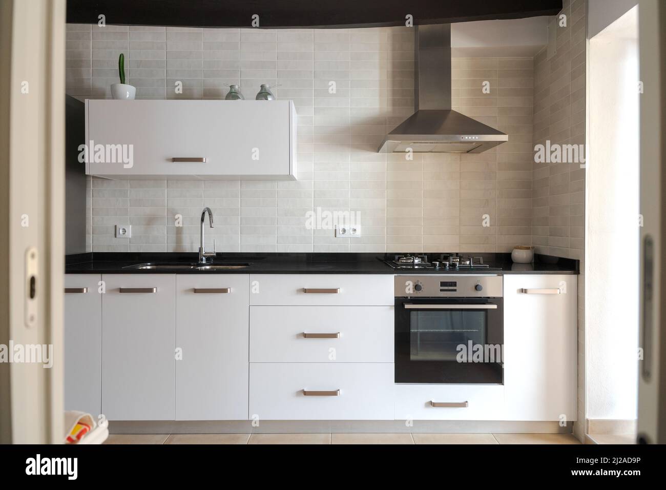 Cucina bianca con luce naturale. Mobili bianchi in marmo nero. Immagine incorniciata con una cornice porta. Piano cottura a gas e ventola estrattore in acciaio inox. Foto Stock