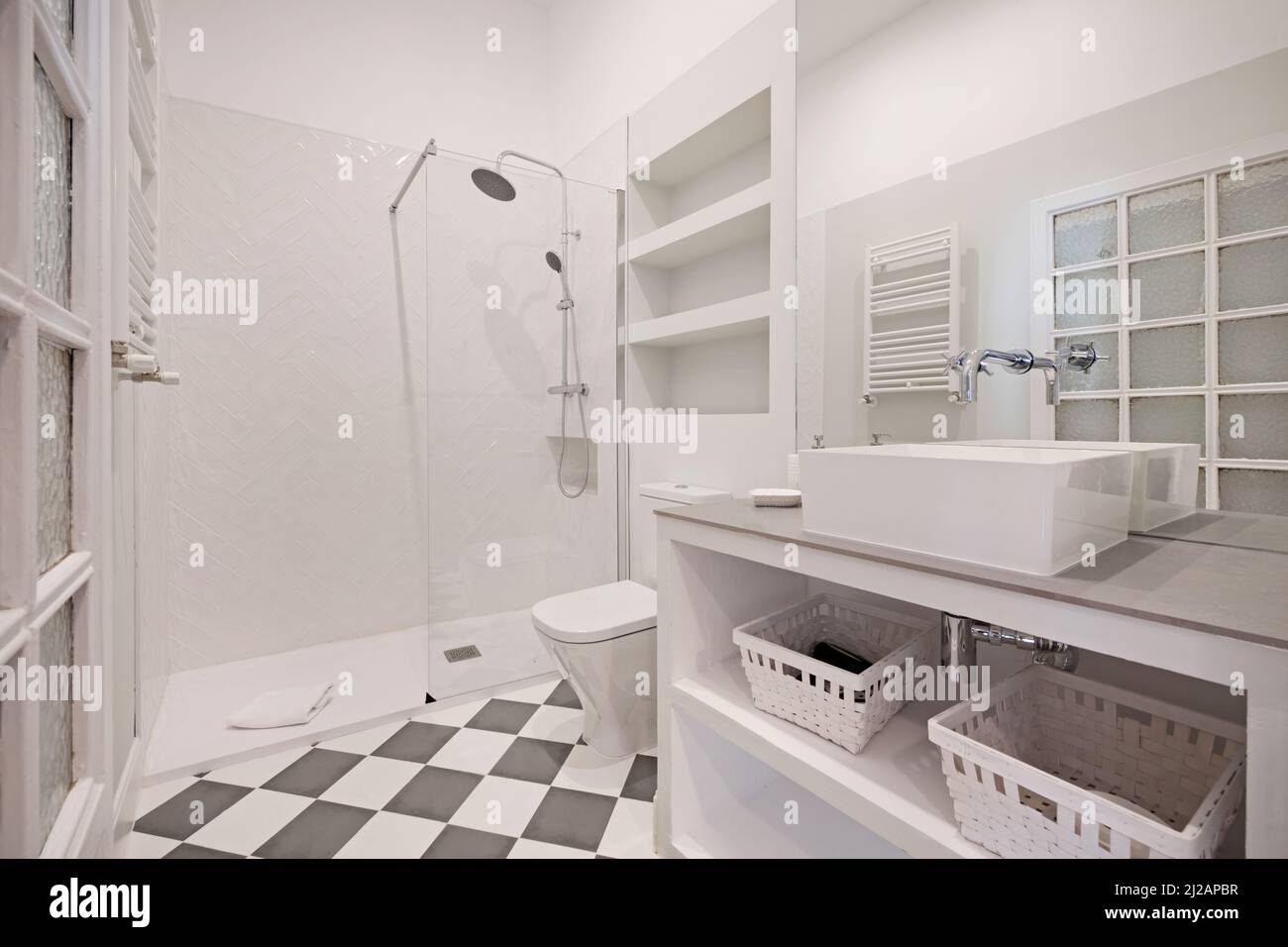 WC con lavabo incorporato con lavabo in porcellana bianca, cestini in vimini, specchio senza telaio e cabina doccia, porta in legno opaca Foto Stock