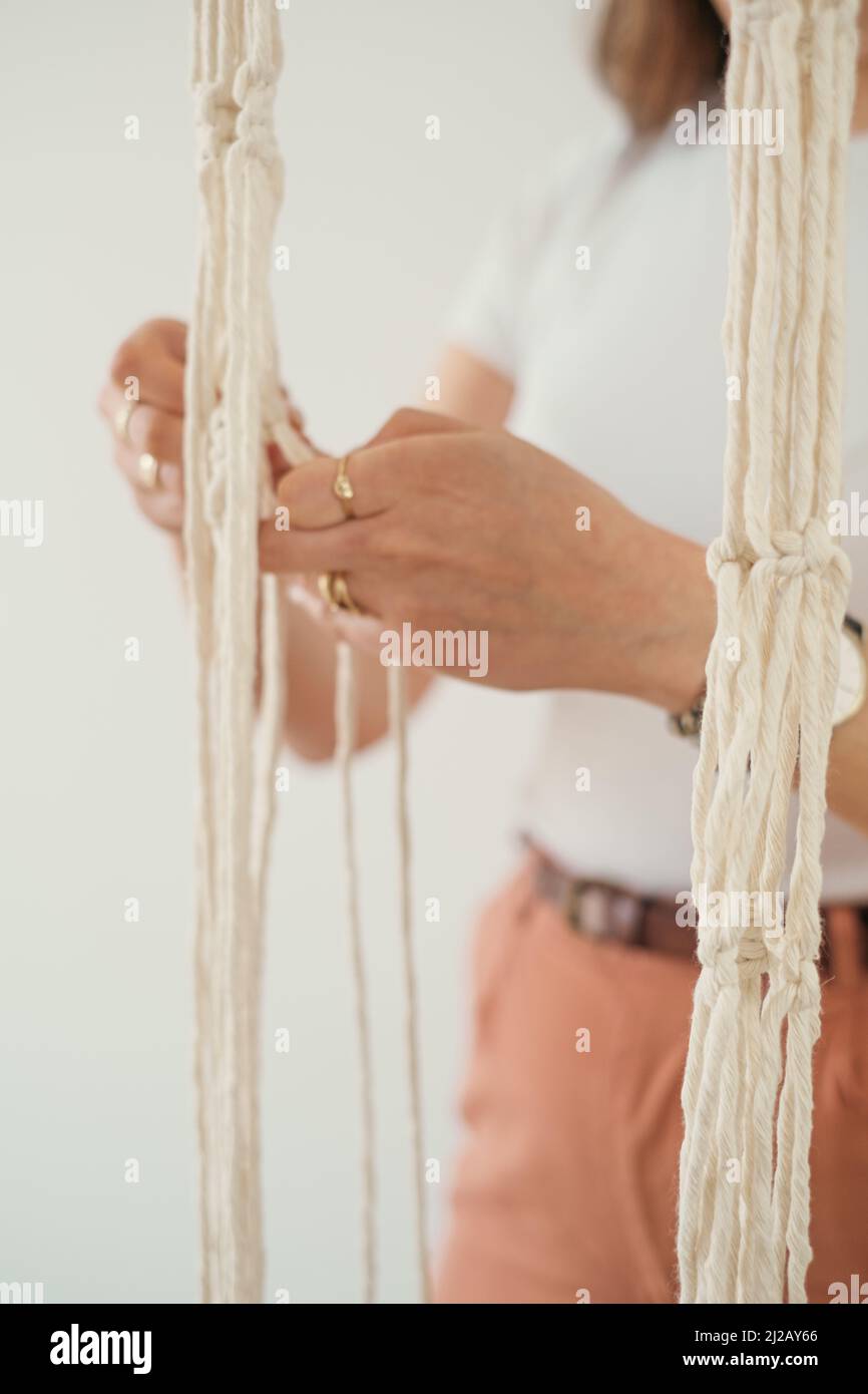 Le mani delle donne tessono un portavetrini di fiore in macrame Boho stile cravatte nodi fili di cotone per creare pizzo Foto Stock