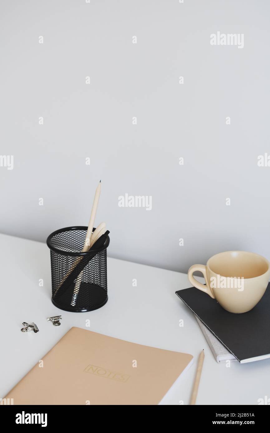 Scrivania in stile minimalista con notebook beige, tazza di tè, cancelleria per ufficio. Spazio di lavoro moderno ed elegante. Foto Stock