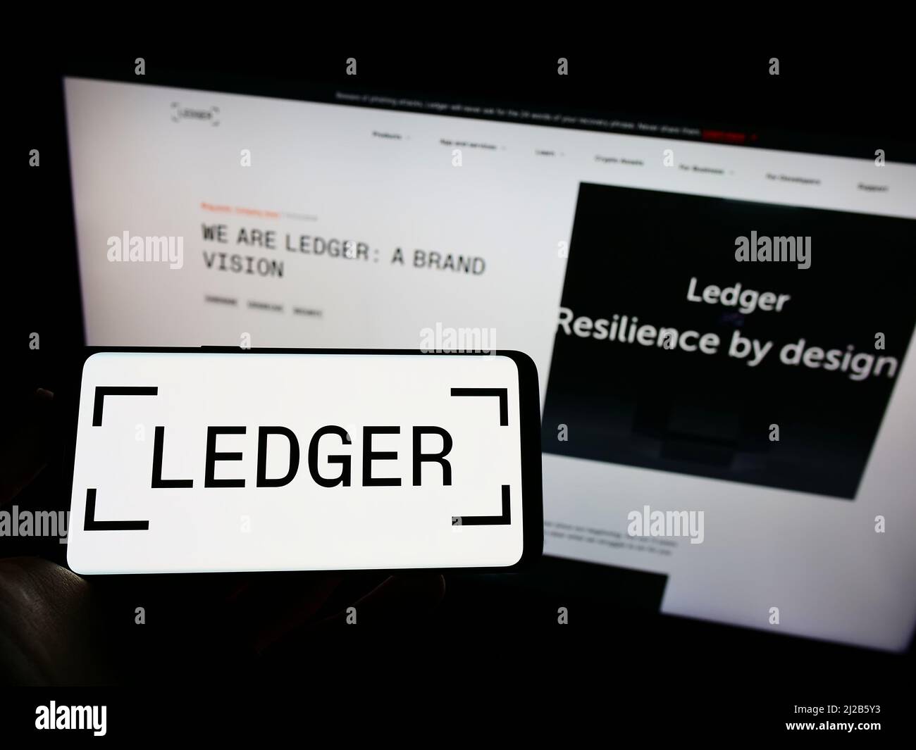 Persona che tiene il cellulare con il logo della società francese di asset digitali Ledger SAS sullo schermo di fronte al sito web aziendale. Mettere a fuoco sul display del telefono. Foto Stock