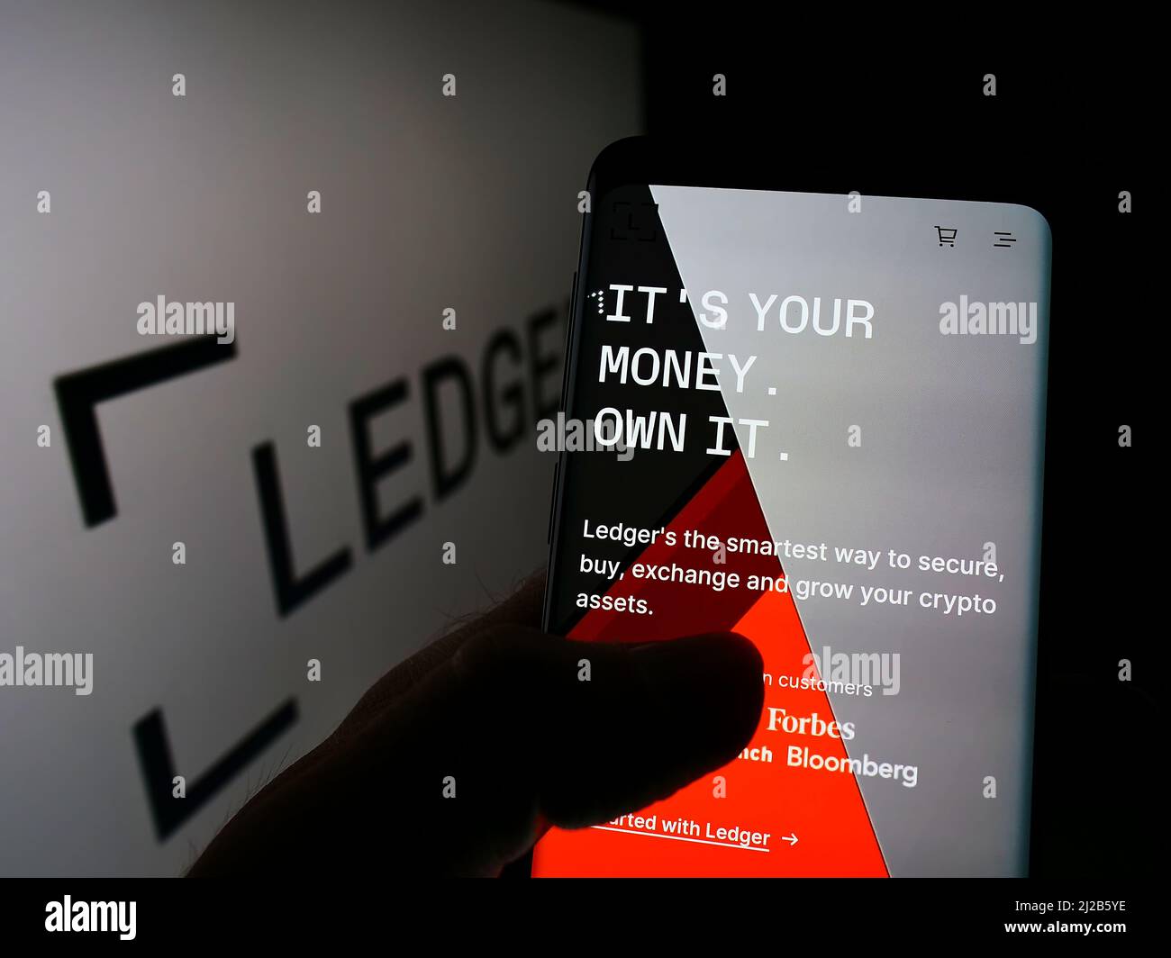 Persona che detiene il cellulare con il sito web della società francese di asset digitali Ledger SAS sullo schermo di fronte al logo. Concentrarsi sul centro del display del telefono. Foto Stock