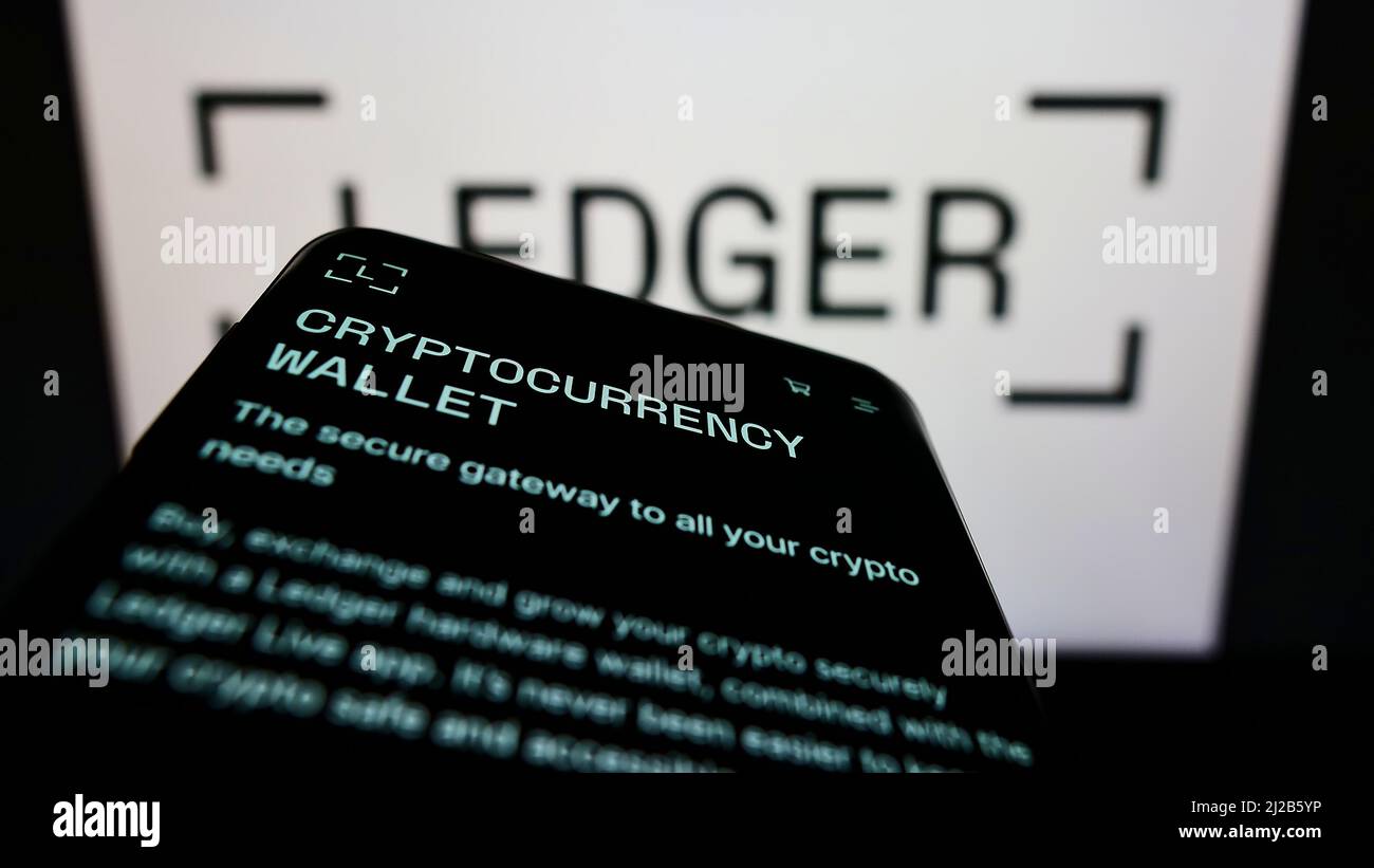 Telefono cellulare con pagina web della società francese di asset digitali Ledger SAS sullo schermo di fronte al logo aziendale. Mettere a fuoco sulla parte superiore sinistra del display del telefono. Foto Stock