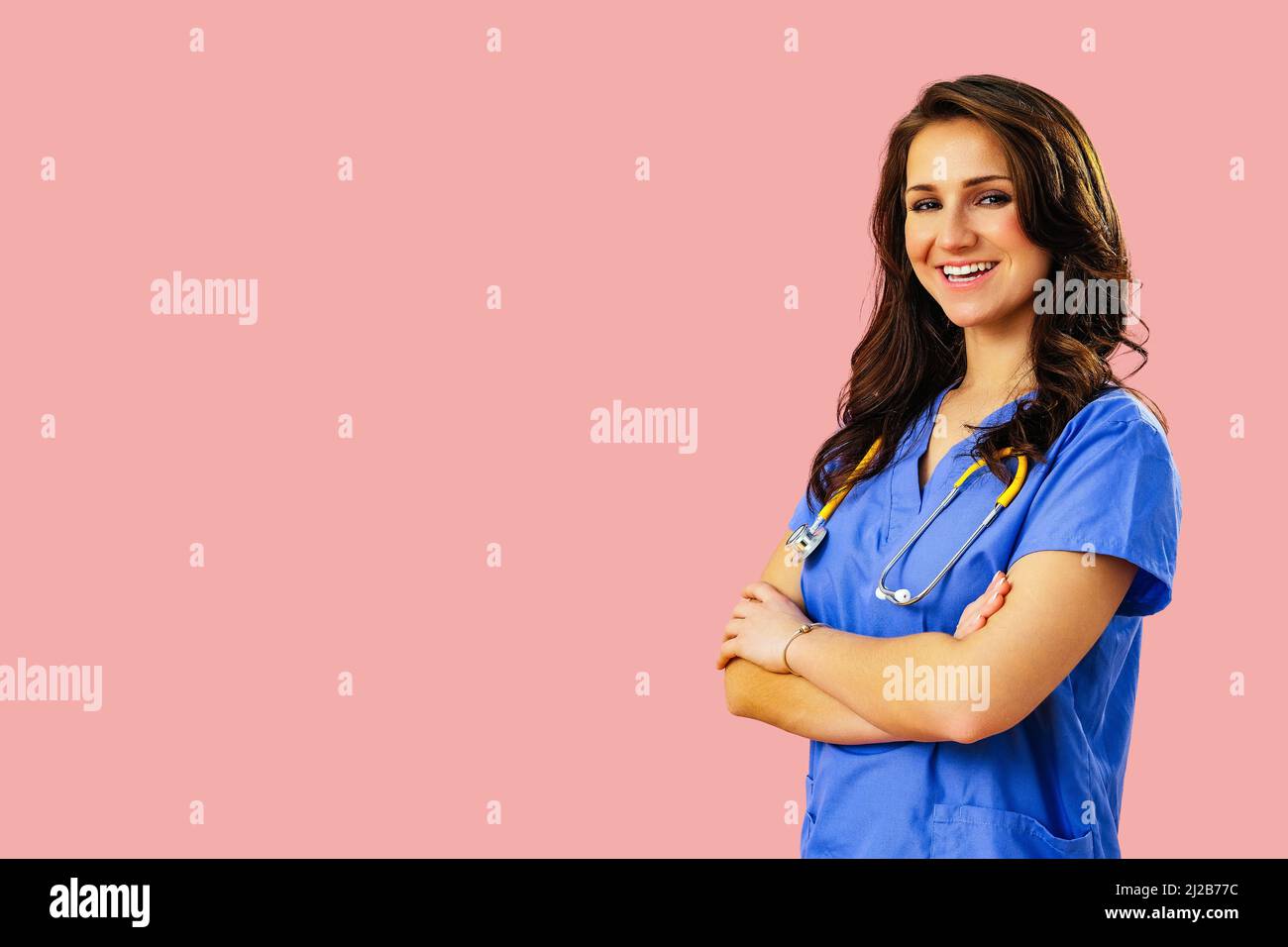 Ritratto di sorridente medico o infermiera in uniforme blu con le braccia incrociate su sfondo rosa studio medico curante Foto Stock