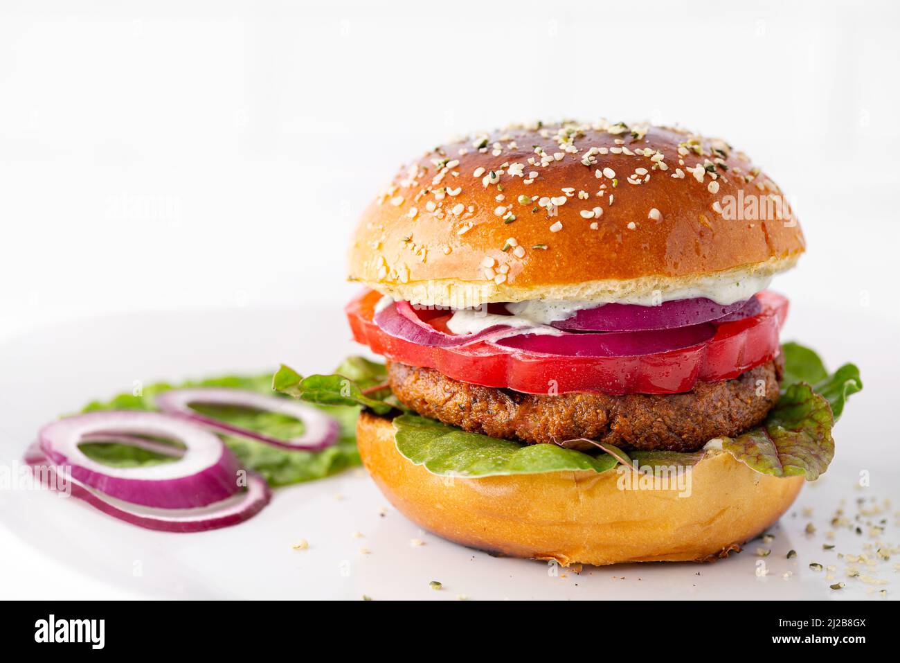 Veggie Burger a base di piante con un pomodoro rosso, cipolla rossa e verdi frondosi su sfondo chiaro; spazio copia Foto Stock