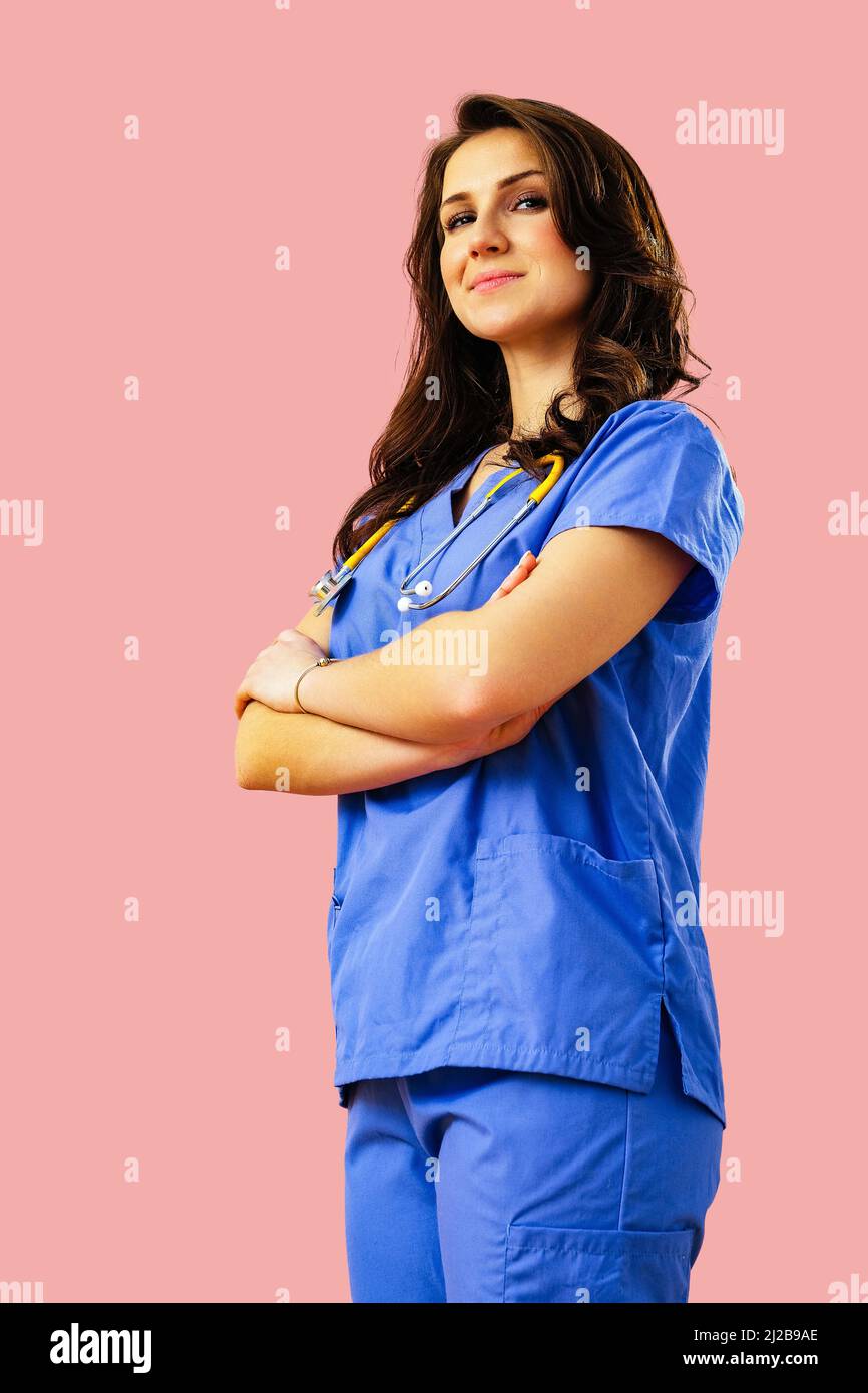 Ritratto di sorridente medico o infermiera in uniforme blu con le braccia incrociate su sfondo rosa studio medico curante Foto Stock